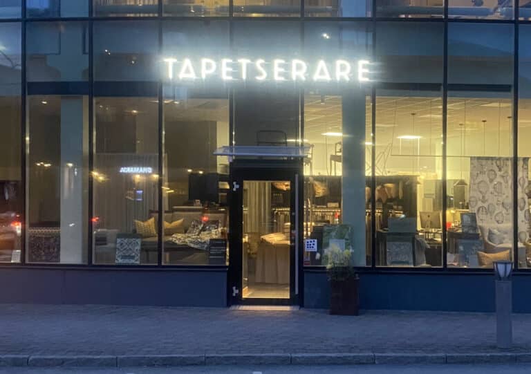 Husfasad med lysande skylt nattetid. Text: Tapetserare