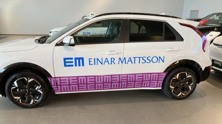 Vit bil med text EM mattsson och en lila bård.