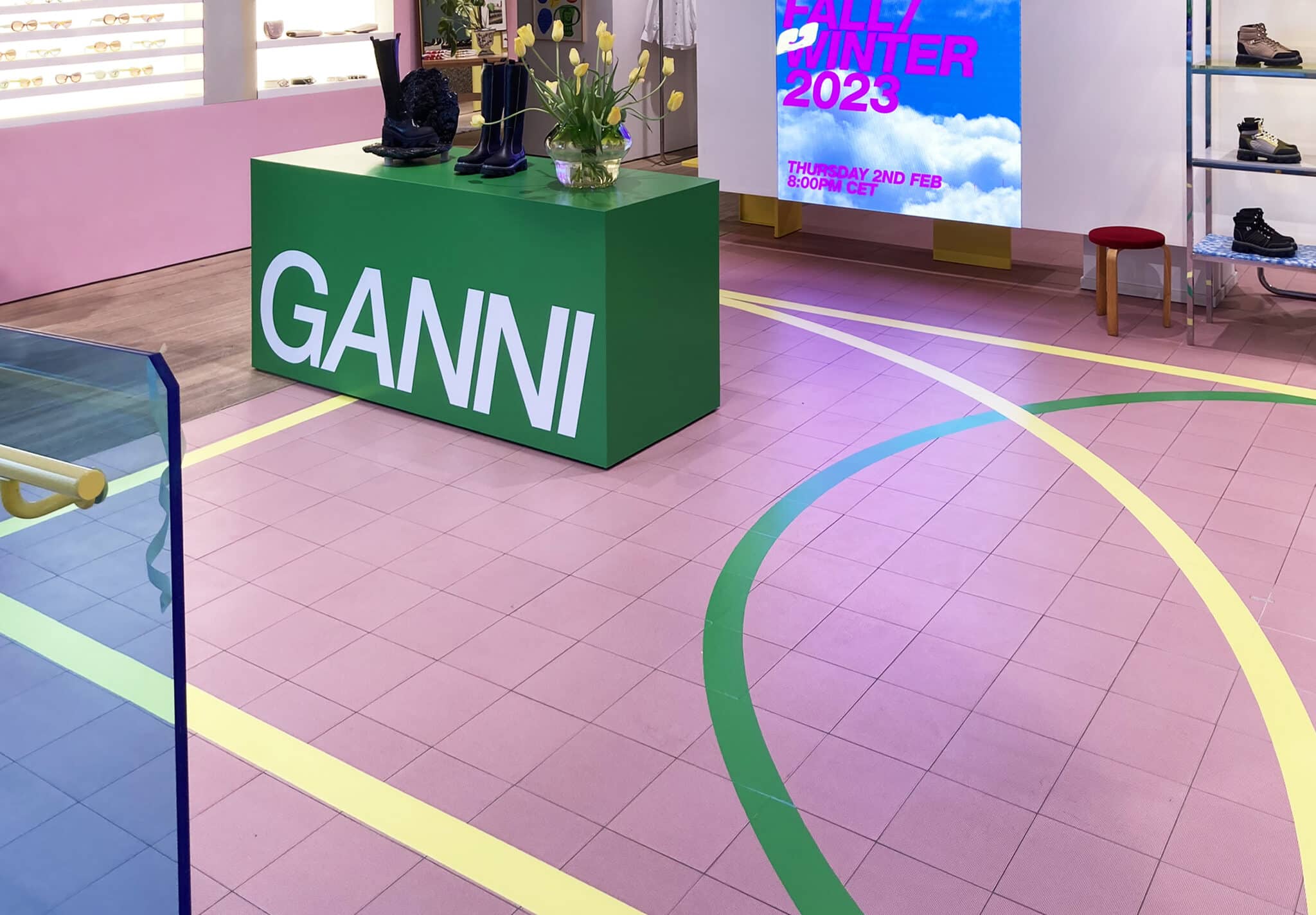 Golv med linjer i gult och grönt. Disk i grönt med texten Ganni i vitt.